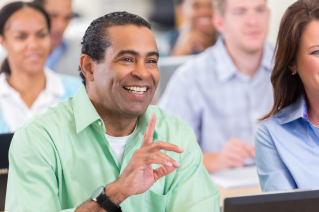 Mature African American businessman raises his hand to ask a question during seminar or continuing education course.